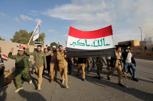 Protesters and militia fighters carry an Iraqi flag outside the U.S. Embassy during a protest to condemn air strikes on bases belonging to Hashd al-Shaabi (paramilitary forces), in Baghdad, Iraq January 1, 2020. REUTERS/Khalid al-Mousily