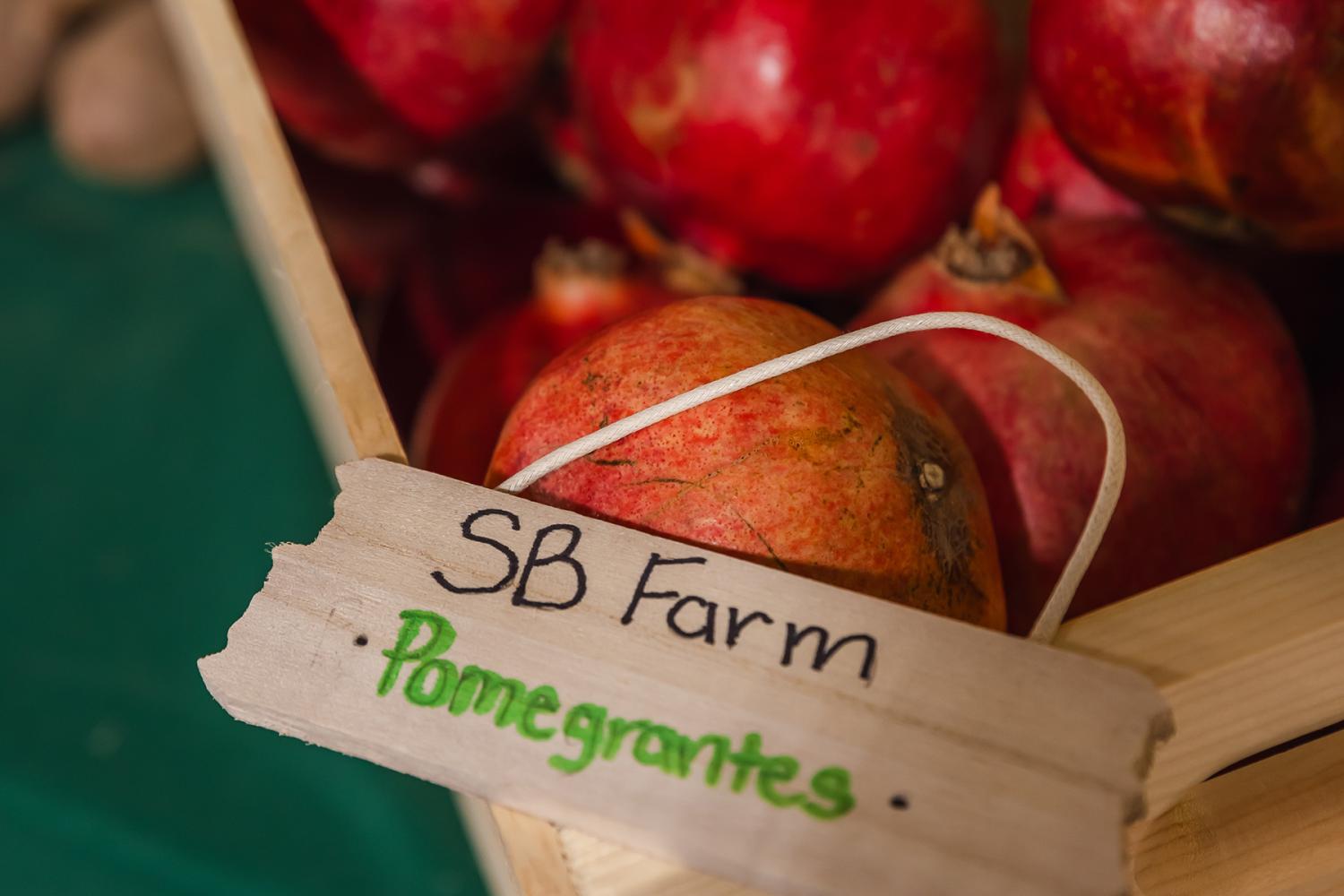 Pomegrantes in wooden bin with small wooden sign reading "SB Farms - Pomegrantes"