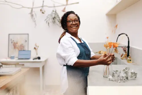 Mature female florist smiles while working on a creative flower arrangement in her own small business, showcasing her craft and enthusiasm for the entrepreneurial journey.