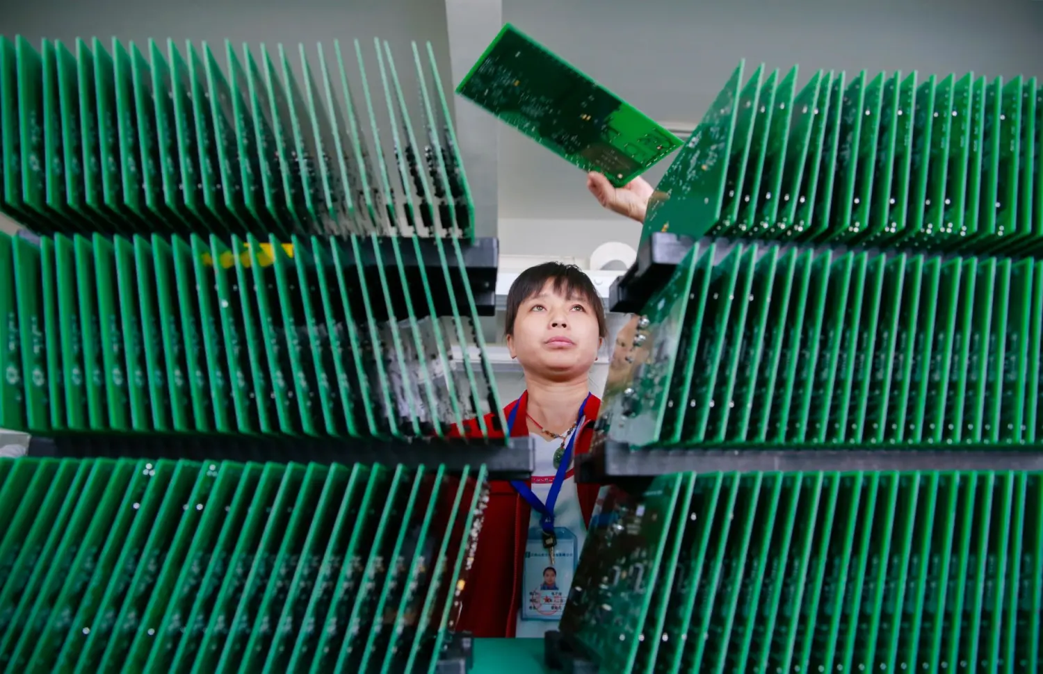 A female industrial worker places the final circuit board on top of a large stack.