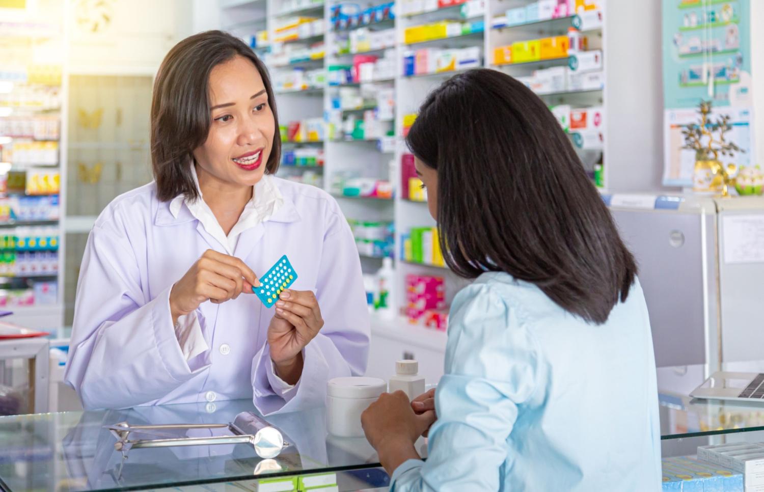 A pharmacist holding a package of birth control pills while speaking to a patient