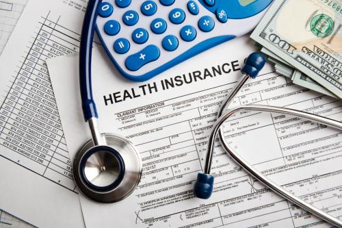Health insurance forms with a calculator, stethoscope, and U.S. dollar bills laying over them.