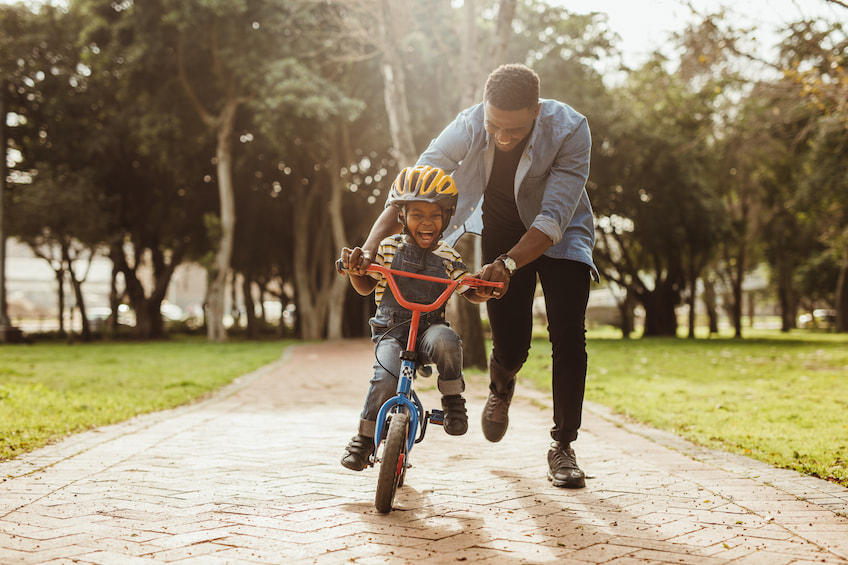 Boy learning to ride a bicycle with his father in park. Father teaching his son cycling at park. Credit: Shutterstock/Jacob Lund