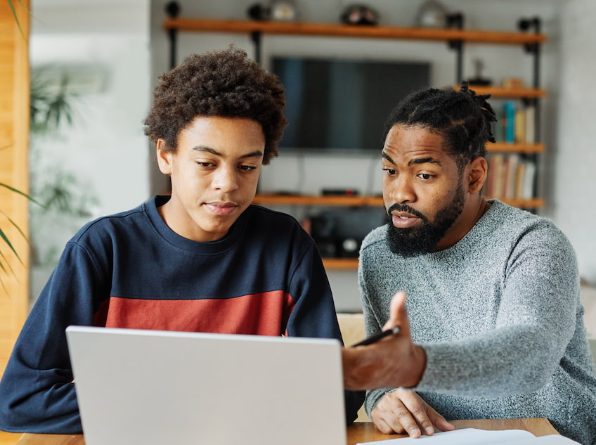 Father and son doing homework with laptop at home.