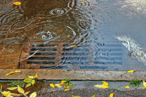 Flooding across road during rain, blocked street drain. Plumbing problems in the city, clogged drain, water flooding. Large puddle due to clogged storm drain. Selective focus