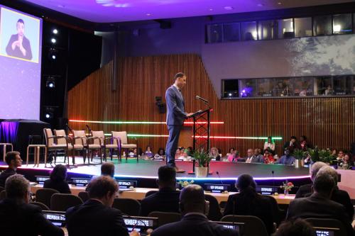 A man stands behind a podium on a stage surrounded by seats