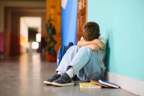 Little boy is shown sitting alone on floor outside of his classroom.