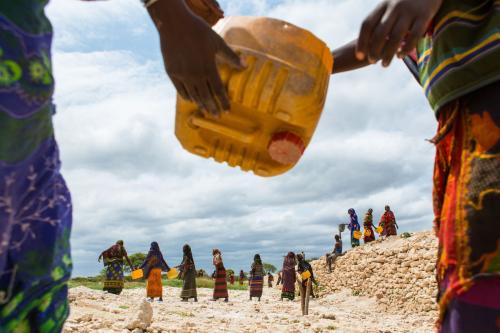 One woman passes a water can to another in the foreground while a line of women work together in the background