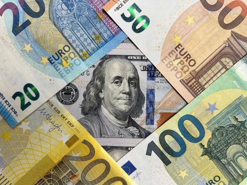 Euro notes lay on top of a $100 bill, framing Ben Franklin's portrait